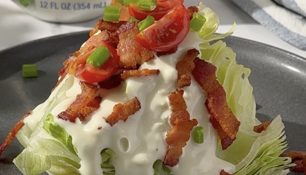 Wedge of iceberg lettuce with Blue Cheese Dressing, bacon and tomatoes.